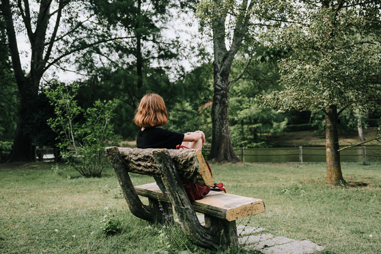 Woman sitting quietly on a park bench surrounded by nature