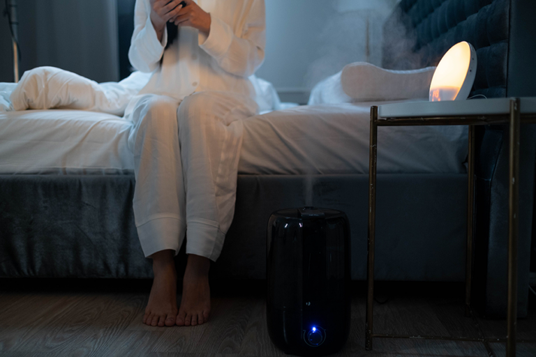 Woman sitting on a bed in a bedroom beside a glowing sunrise alarm clock