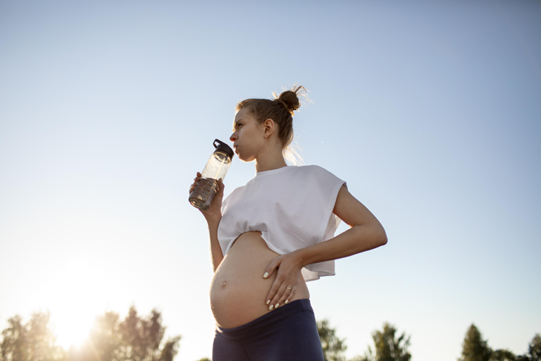 Pregnant woman drinking water outdoors on a warm day