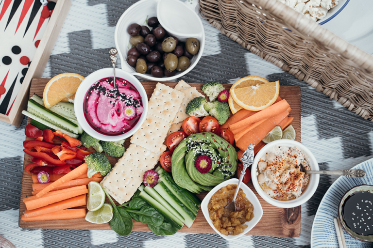 Healthy snack board with vegetables, avocado, dips, crackers, olives, and fruit