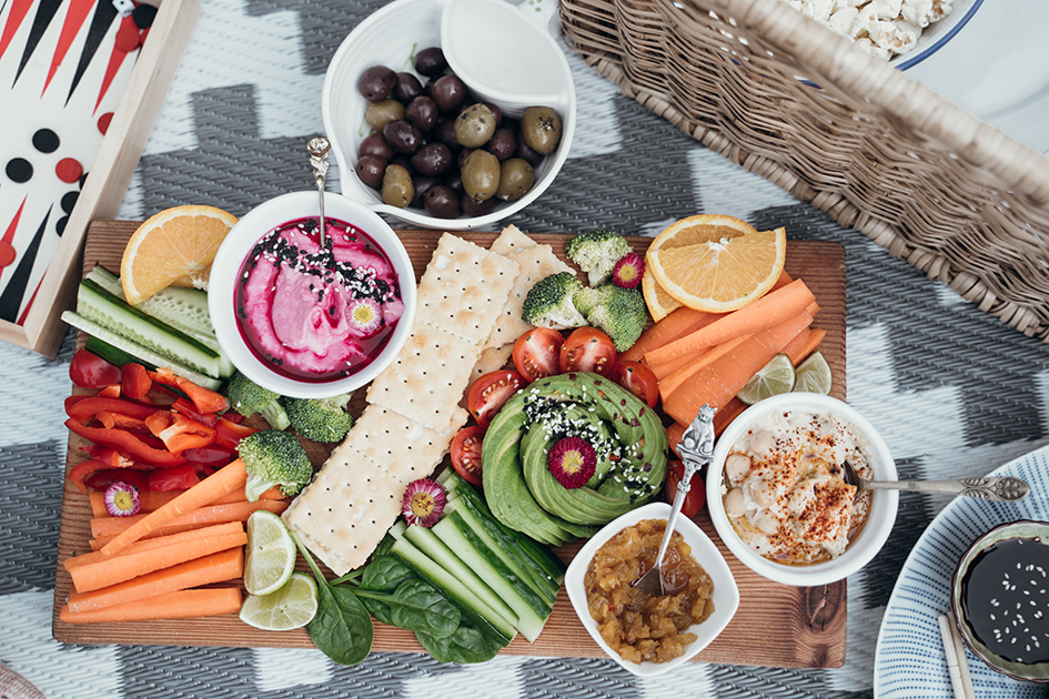 Healthy snack board with vegetables, avocado, dips, crackers, olives, and fruit