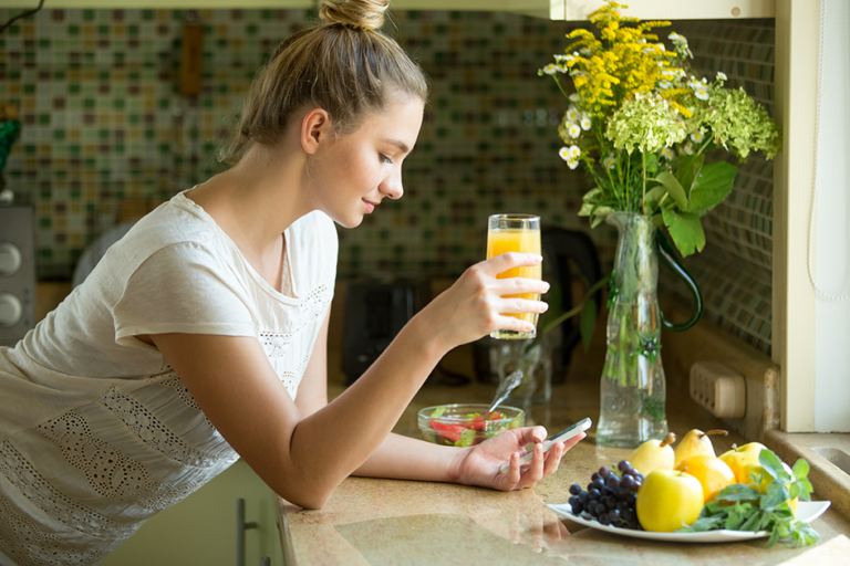 Woman enjoying a healthy morning routine with fresh fruit, orange juice, and natural sunlight to support hormone balance and overall wellness