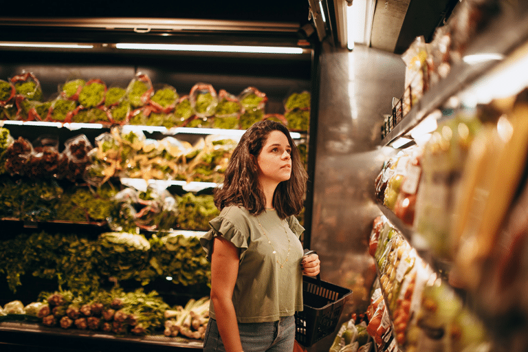 Woman standing in a grocery store aisle, thoughtfully choosing between food products, illustrating decision fatigue and the mental effort of making everyday choices