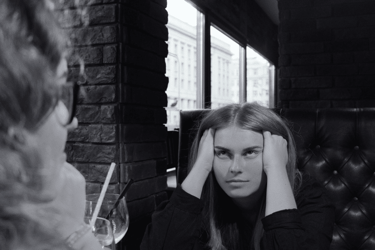 Young woman holding her head in her hands during a difficult conversation at a café