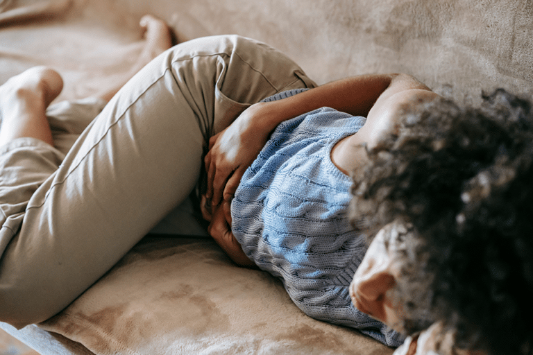 Woman lying on sofa holding her stomach with digestive discomfort