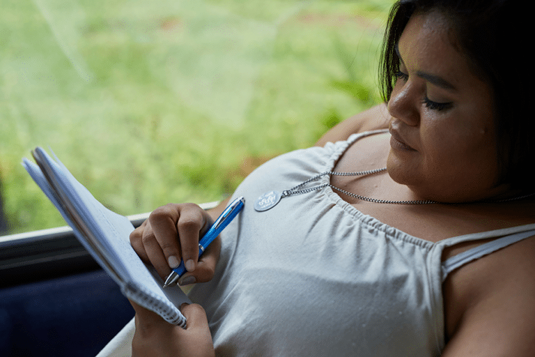 Woman writing in a journal by the window, tracking changes in energy, mood, cravings, and menstrual cycle patterns