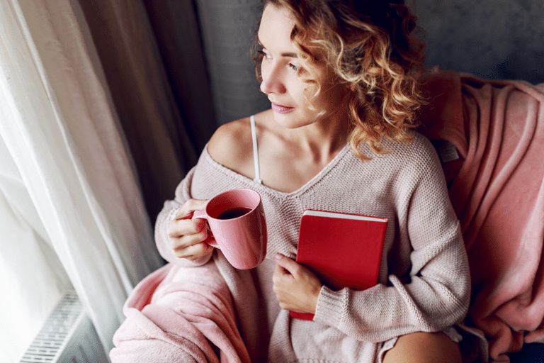Woman in her 40s sitting by a window with tea and a journal