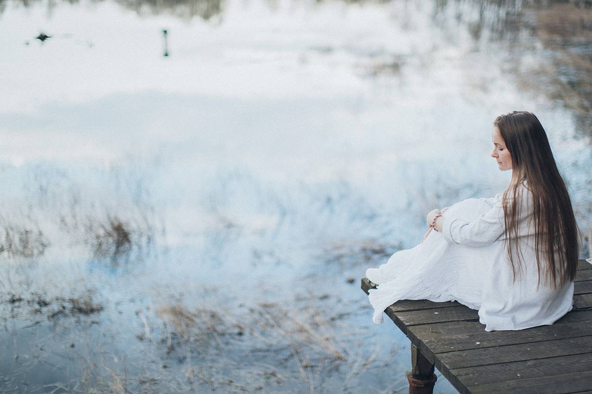 Woman sitting quietly on a wooden dock beside a calm lake, enjoying a peaceful moment in nature