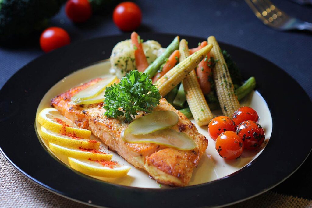 Grilled salmon fillet with lemon, cherry tomatoes, baby corn, and mixed vegetables