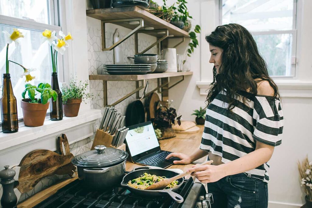 Woman cooking dinner while using a laptop in her kitchen