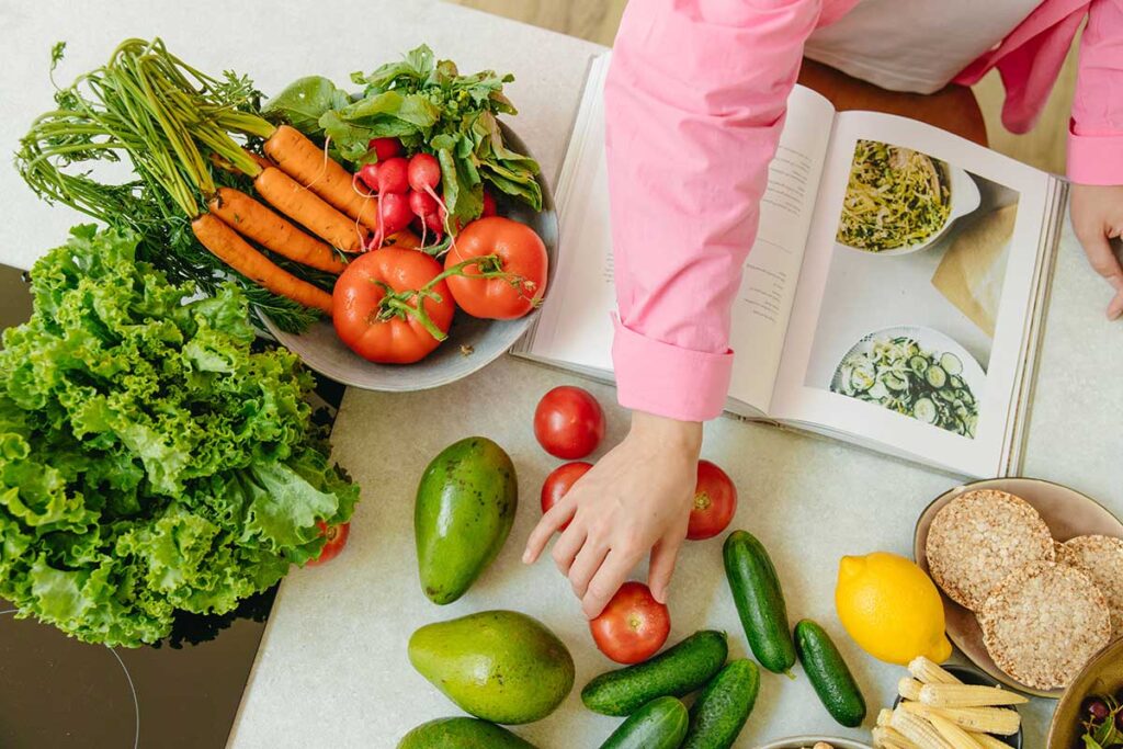 Woman using a cookbook while preparing fresh vegetables for a healthy meal