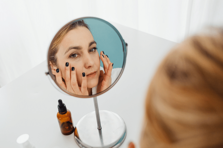 Woman examining her complexion in a bathroom mirror because her skin still looks dull despite a regular skincare routine