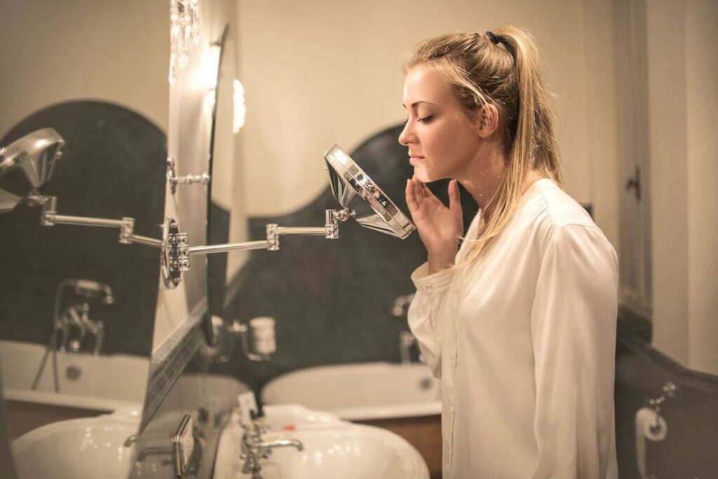 Blonde woman in her 40s examining sensitive facial skin in a small mirror