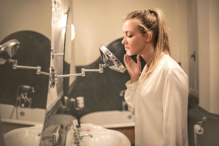 Blonde woman in her 40s examining sensitive facial skin in a small mirror
