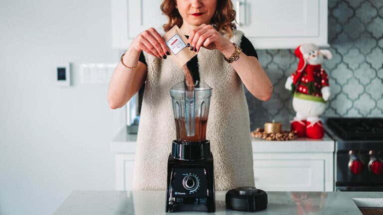 Woman adding powdered supplement to a blender in her kitchen