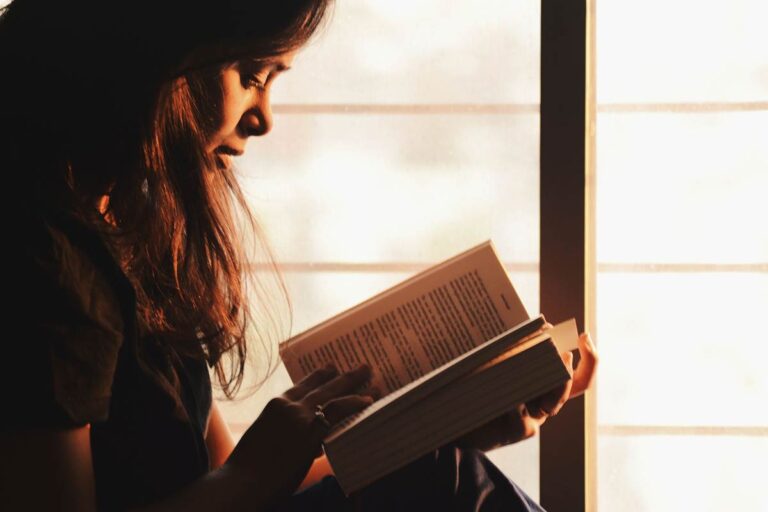 Woman reading a book by a window while exploring healthier boundaries and personal growth