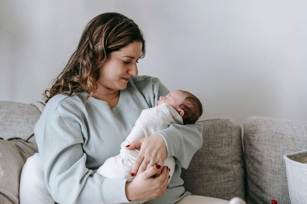 Mother sitting on a sofa and holding her newborn baby close in her arms