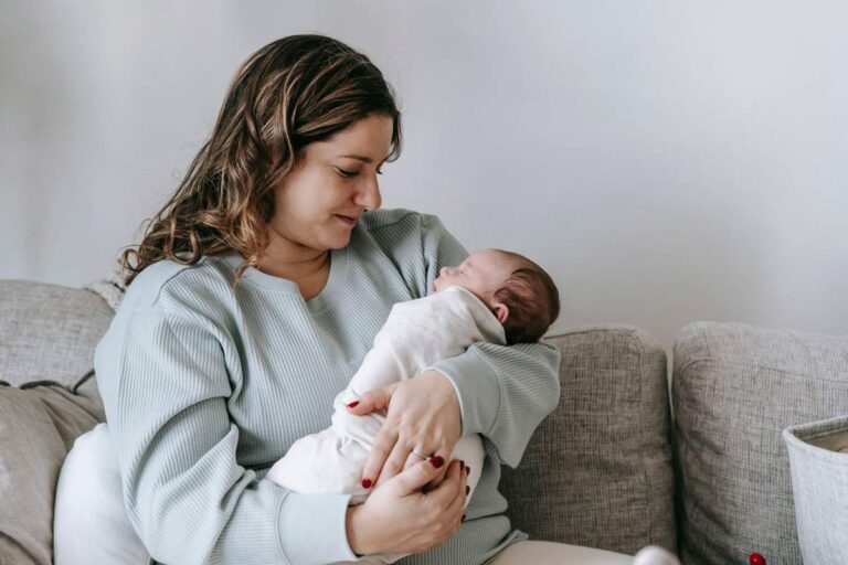 Mother sitting on a sofa and holding her newborn baby close in her arms