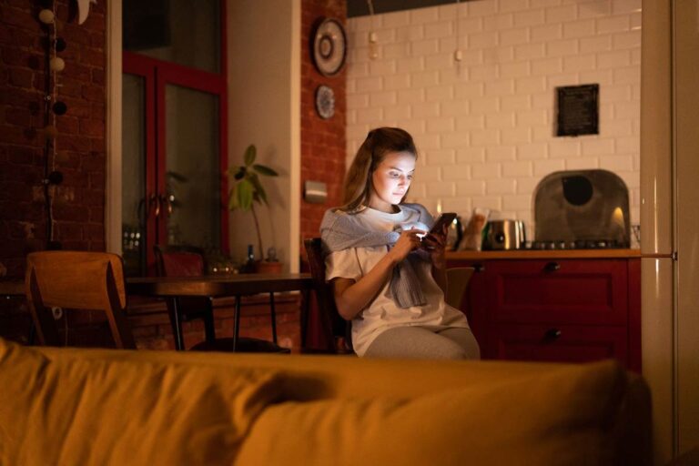 Woman scrolling on her phone while sitting at a dining table in the evening