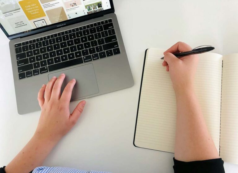 Person working on a laptop and writing in a notebook
