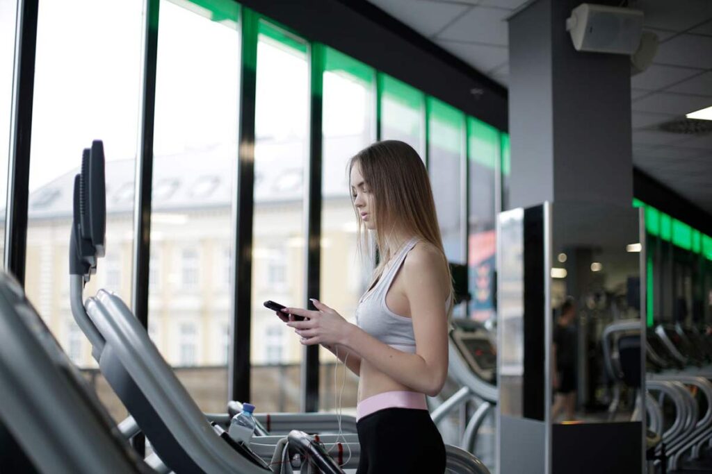 Woman looking at her phone while walking on a treadmill at the gym